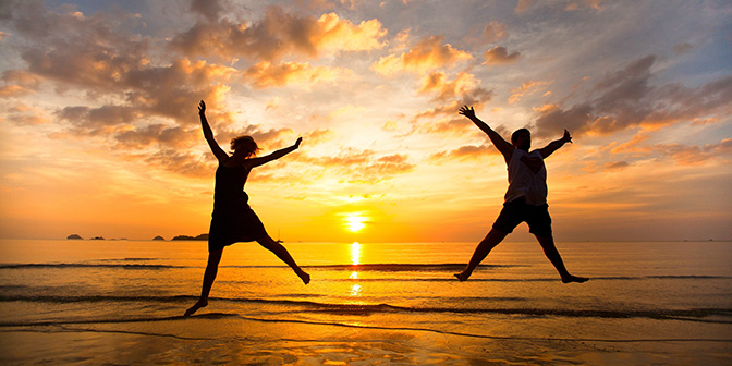 man and woman jump on a beach at sunset